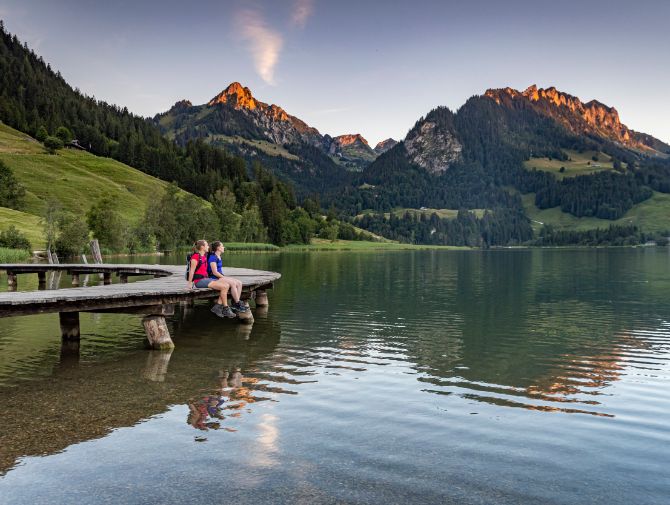 Zwei Wanderer sitzen auf einem Steg am Schwarzsee. 